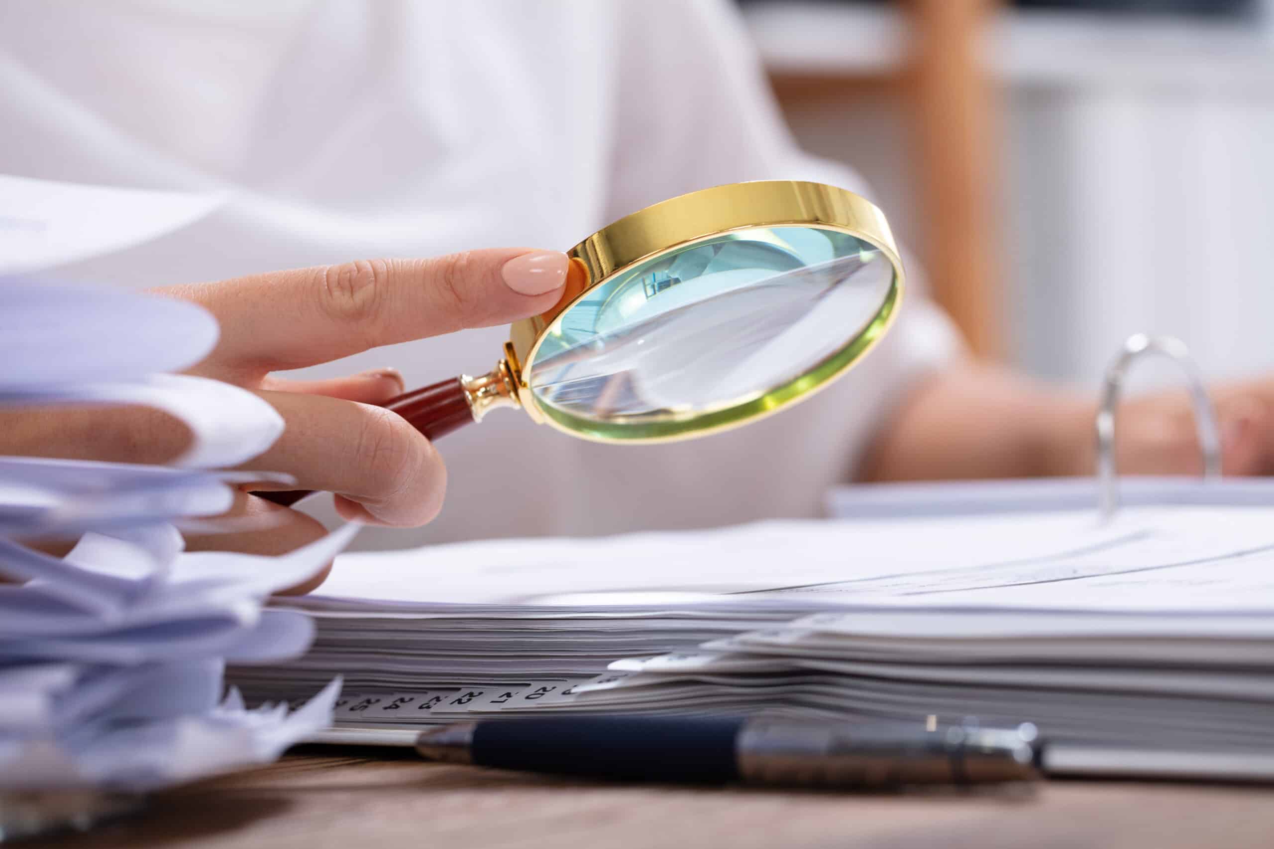 Close-up Of A Businesswoman's Hand Holding Magnifying Glass Over Invoice