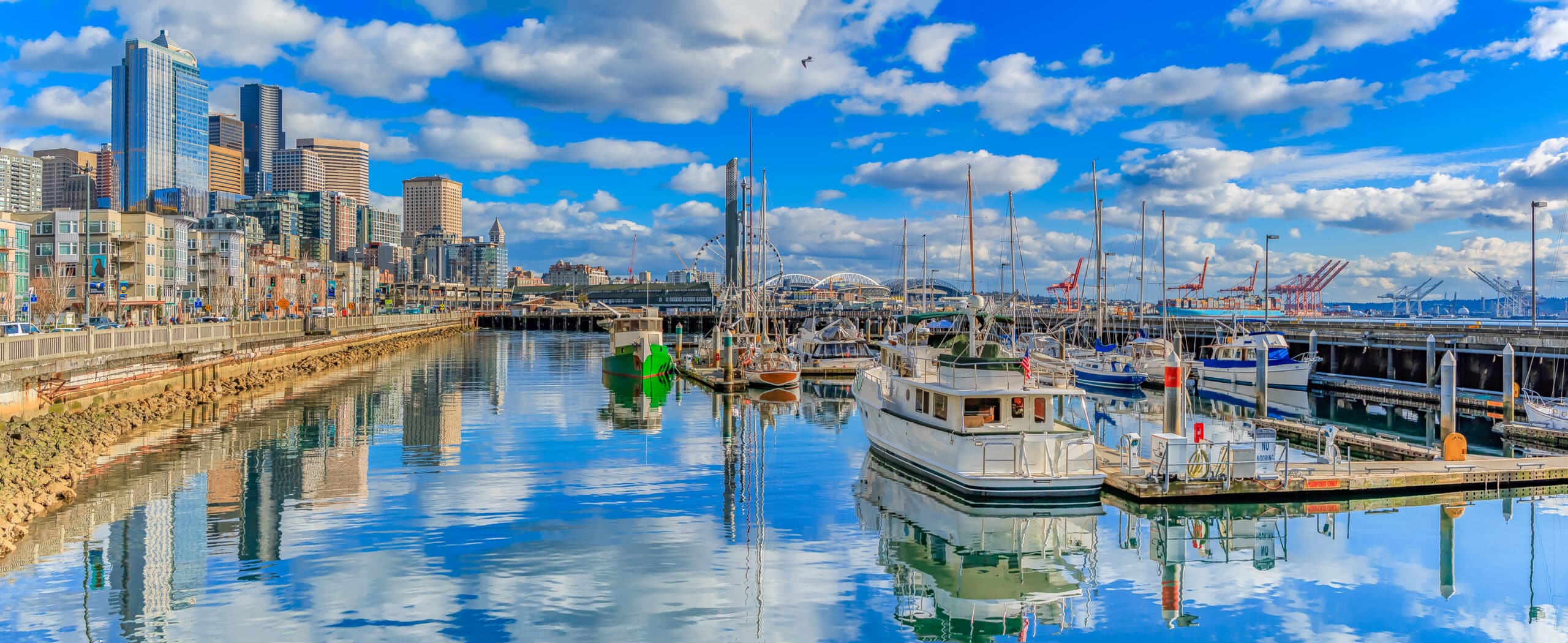 Panoramic view of Seattle waterfront with the skyline of piers, skyscrapers and Ferris wheel on a bright sunny day with clouds